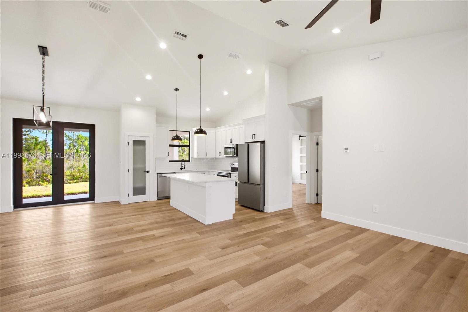 A modern kitchen with white cabinetry and an island opens into a spacious living area — 7322 Granada Boulevard, Sebring FL 33872, SEBRING, FL