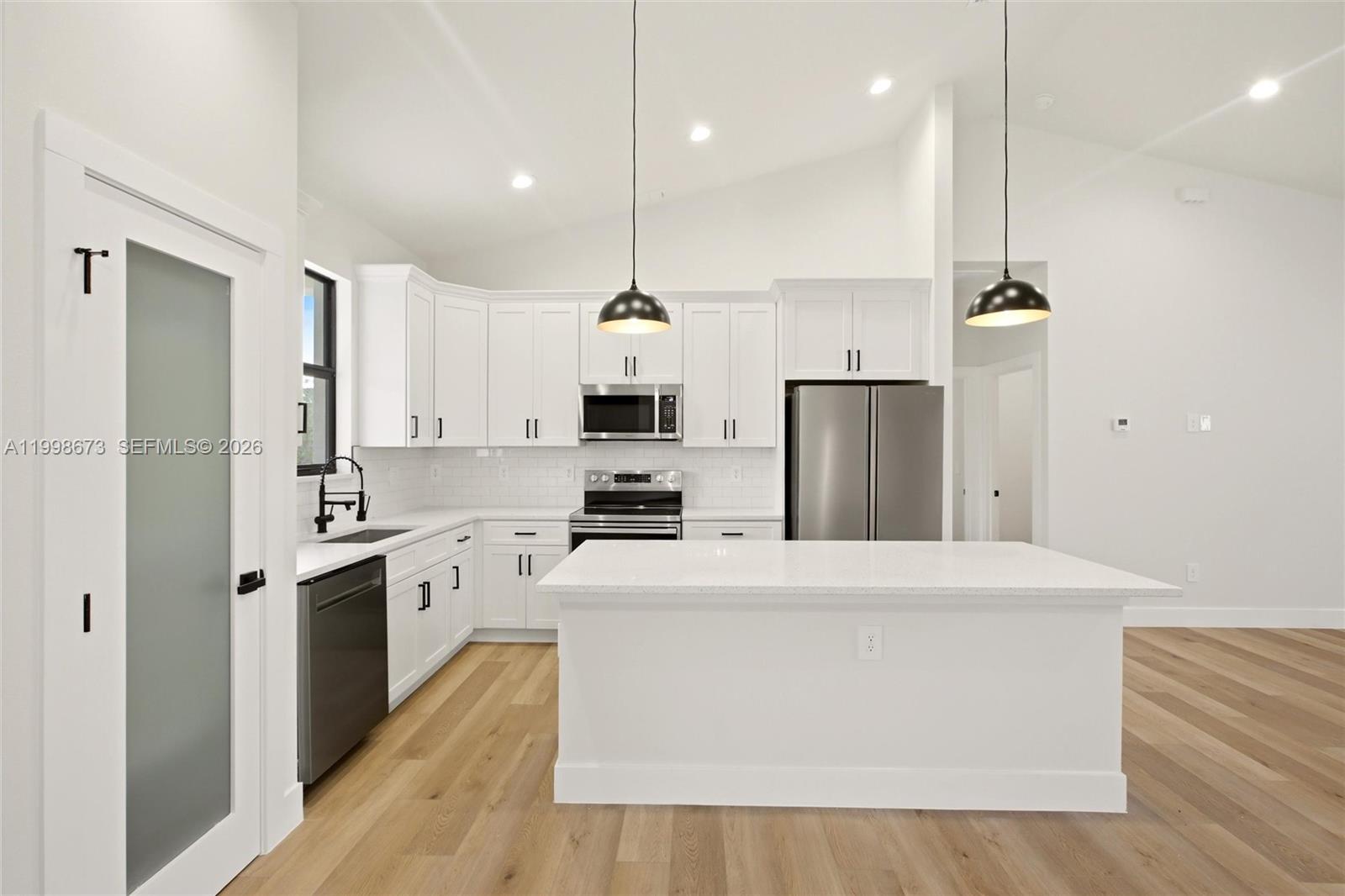 A modern kitchen features white cabinets, stainless steel appliances, a center island, and wood flooring — 7322 Granada Boulevard, Sebring FL 33872, SEBRING, FL