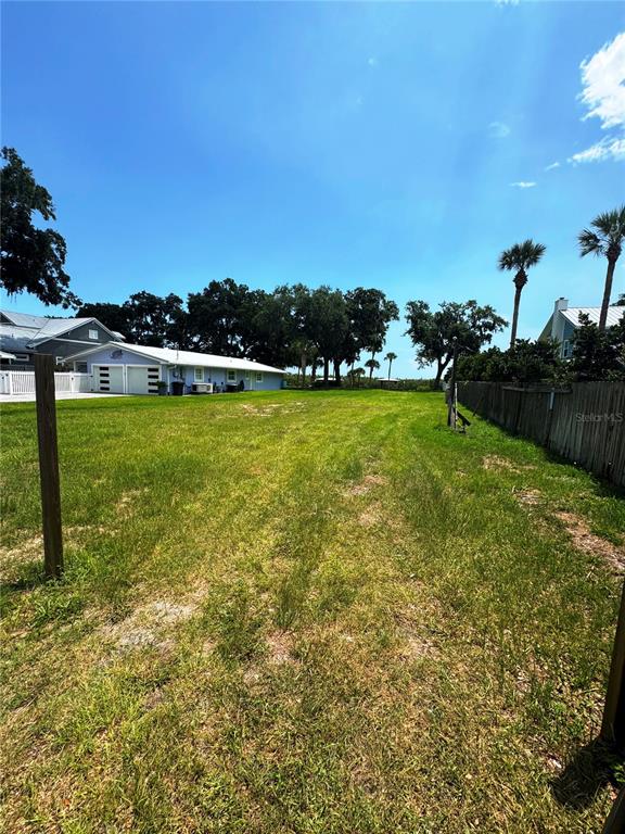 A grassy vacant lot sits in front of a light-colored house under a clear sky — 622 N RIVERSIDE DRIVE, NEW SMYRNA BEACH, FL