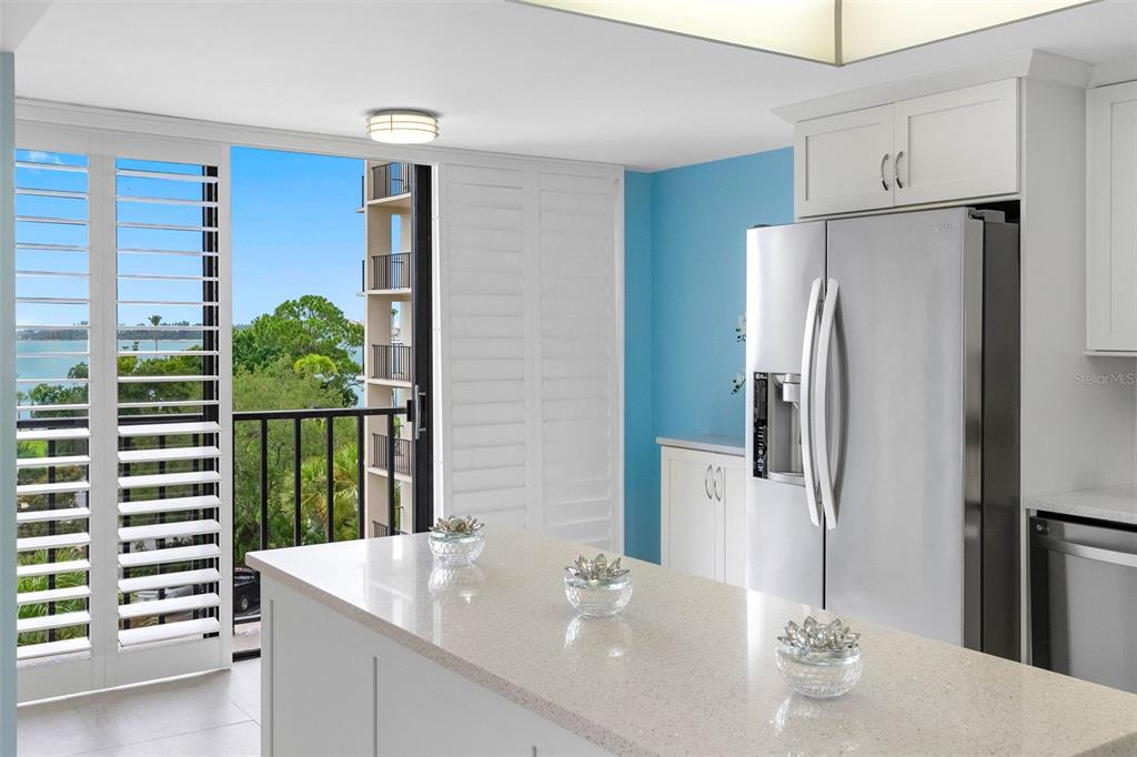 A kitchen island with quartz countertops sits before a balcony overlooking water and trees — 150 BELLEVIEW BOULEVARD UNIT 401, BELLEAIR, FL