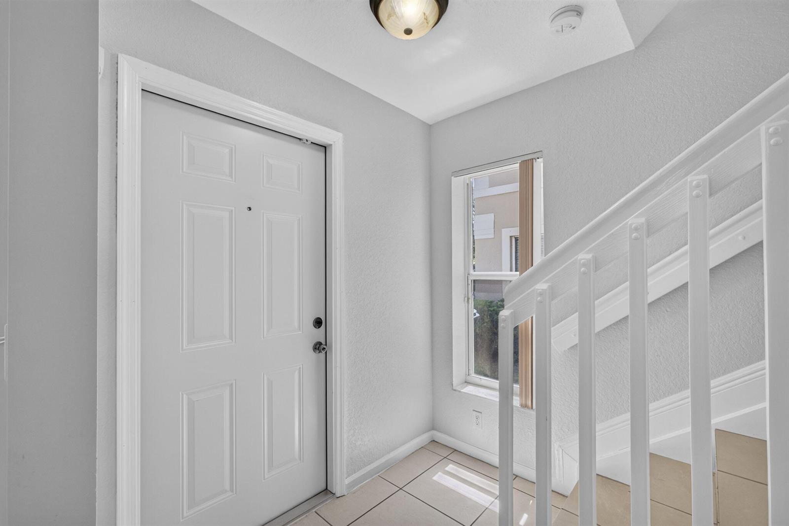 An entryway features a white front door, tiled flooring, and a white staircase railing — 946 Summit Lake Drive, West Palm Beach FL 33406, WEST PALM BEACH, FL