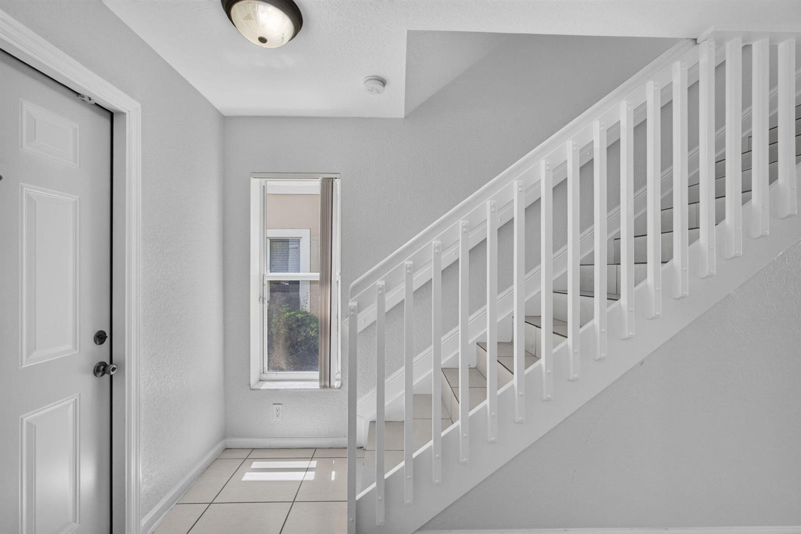 An entryway features white tile flooring, a staircase with a white railing, and a window — 946 Summit Lake Drive, West Palm Beach FL 33406, WEST PALM BEACH, FL