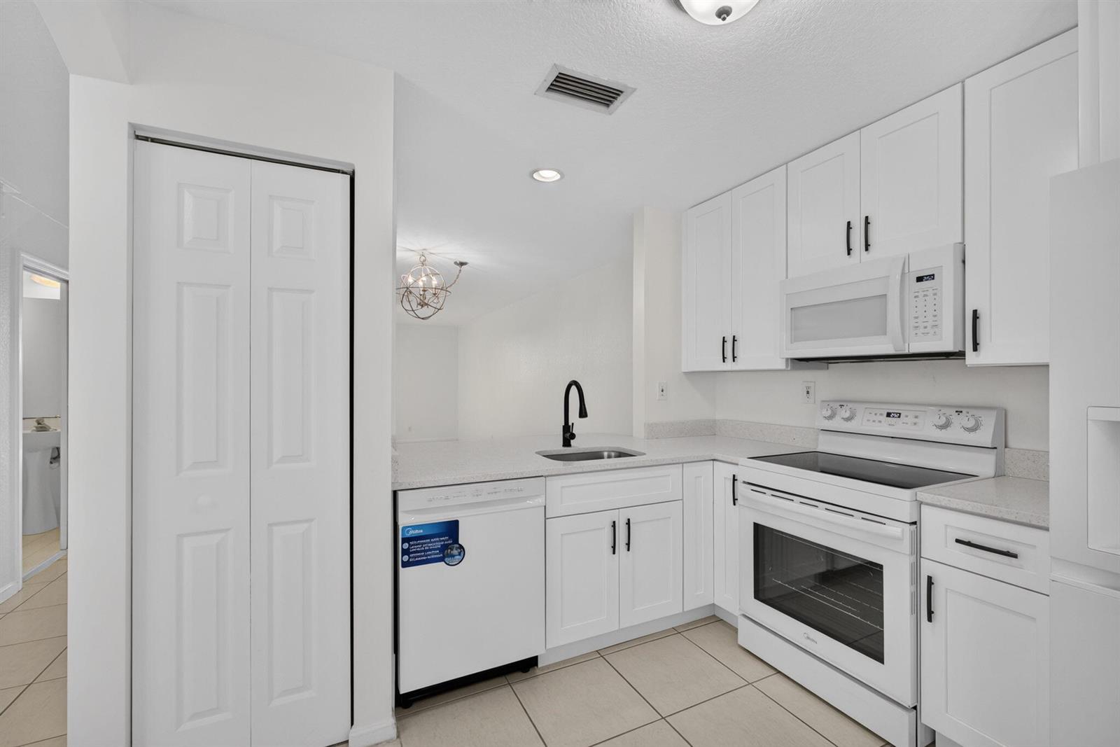 A kitchen features white cabinets, stainless steel appliances, a black faucet, and light tile flooring — 946 Summit Lake Drive, West Palm Beach FL 33406, WEST PALM BEACH, FL