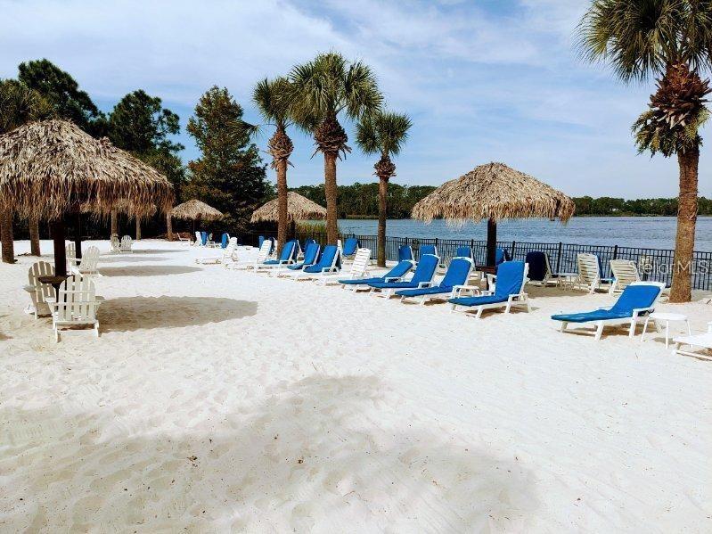 A sandy beach area features palm trees, thatched-roof umbrellas, and rows of blue lounge chairs — 510 RUM RUN UNIT 510, DAVENPORT, FL