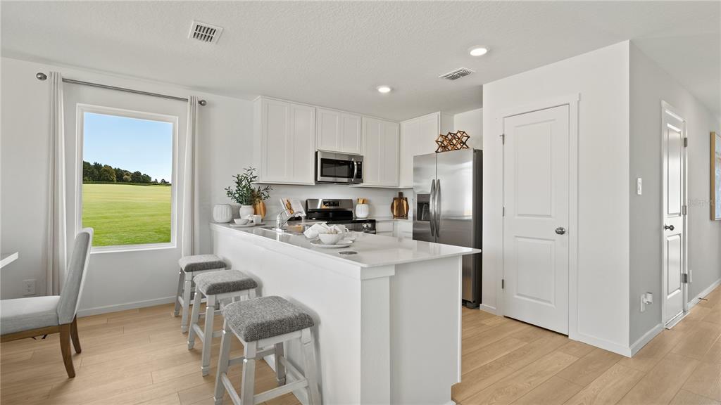 A modern kitchen features white cabinetry, stainless steel appliances, a breakfast bar, and light flooring — 1554 PLANK PLACE, DAVENPORT, FL