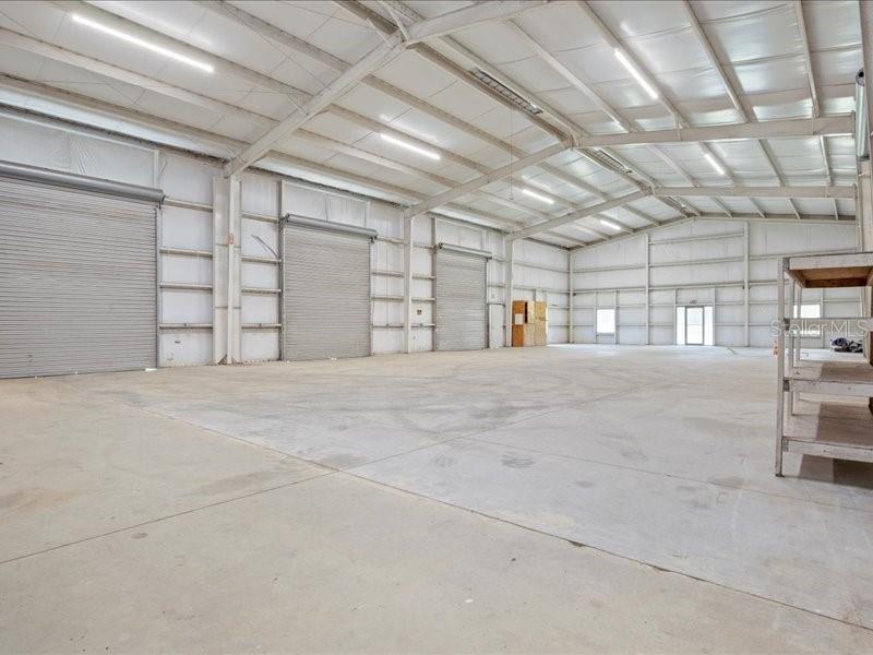 A large, empty industrial warehouse space features concrete floors, metal walls, and roll-up doors — 22429 S US HIGHWAY 441, HIGH SPRINGS, FL