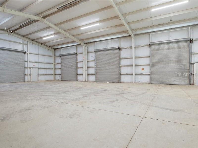 An empty warehouse interior features a concrete floor and three large metal roll-up doors — 22429 S US HIGHWAY 441, HIGH SPRINGS, FL
