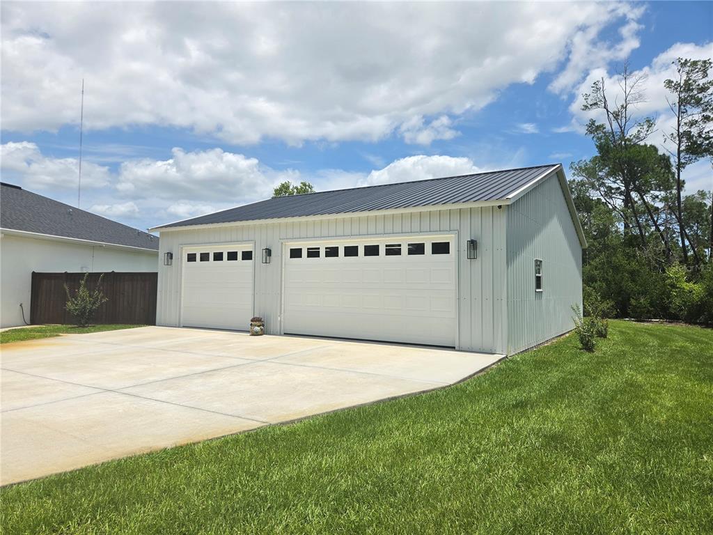 A detached two-car garage with white vertical siding and a dark metal roof — 30658 EAST BLUEBELL AVE, EUSTIS, FL