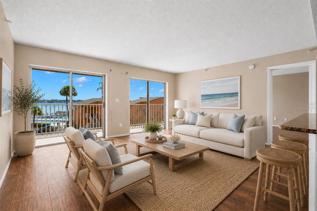 An empty living room features wood-look tile flooring, beige walls, and two sliding glass doors — 7432 SUNSHINE SKYWAY LANE S UNIT 302, ST PETERSBURG, FL