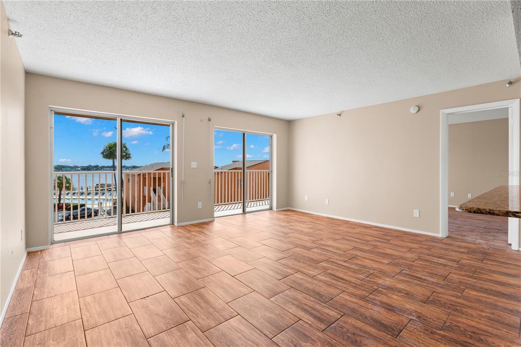 An empty living room with wood-look tile flooring and sliding glass doors leading to a balcony — 7432 SUNSHINE SKYWAY LANE S UNIT 302, ST PETERSBURG, FL