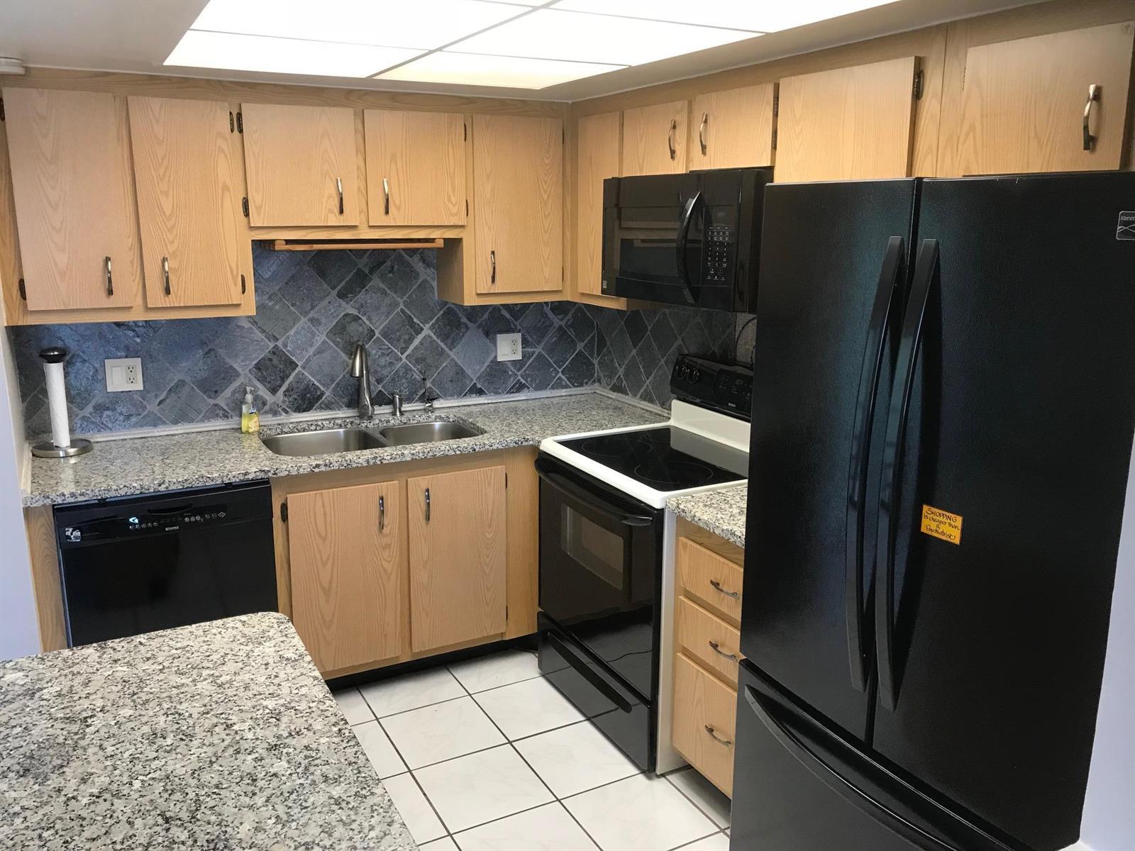 A kitchen featuring light wood cabinets, black appliances, granite countertops, and a gray tiled backsplash — 4147 Oak Terrace Drive, FL 33463, FL