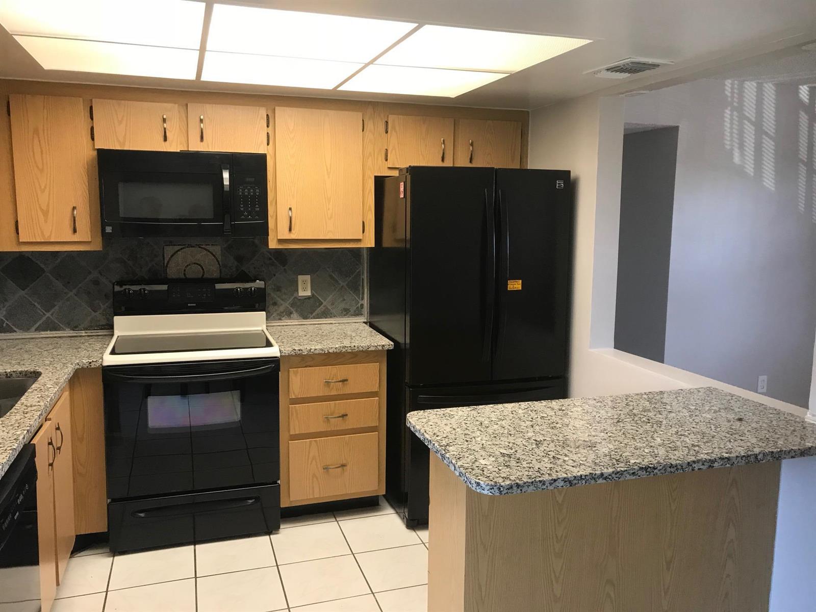 A kitchen features light wood cabinets, black appliances, granite countertops, and white tile flooring — 4147 Oak Terrace Drive, FL 33463, FL