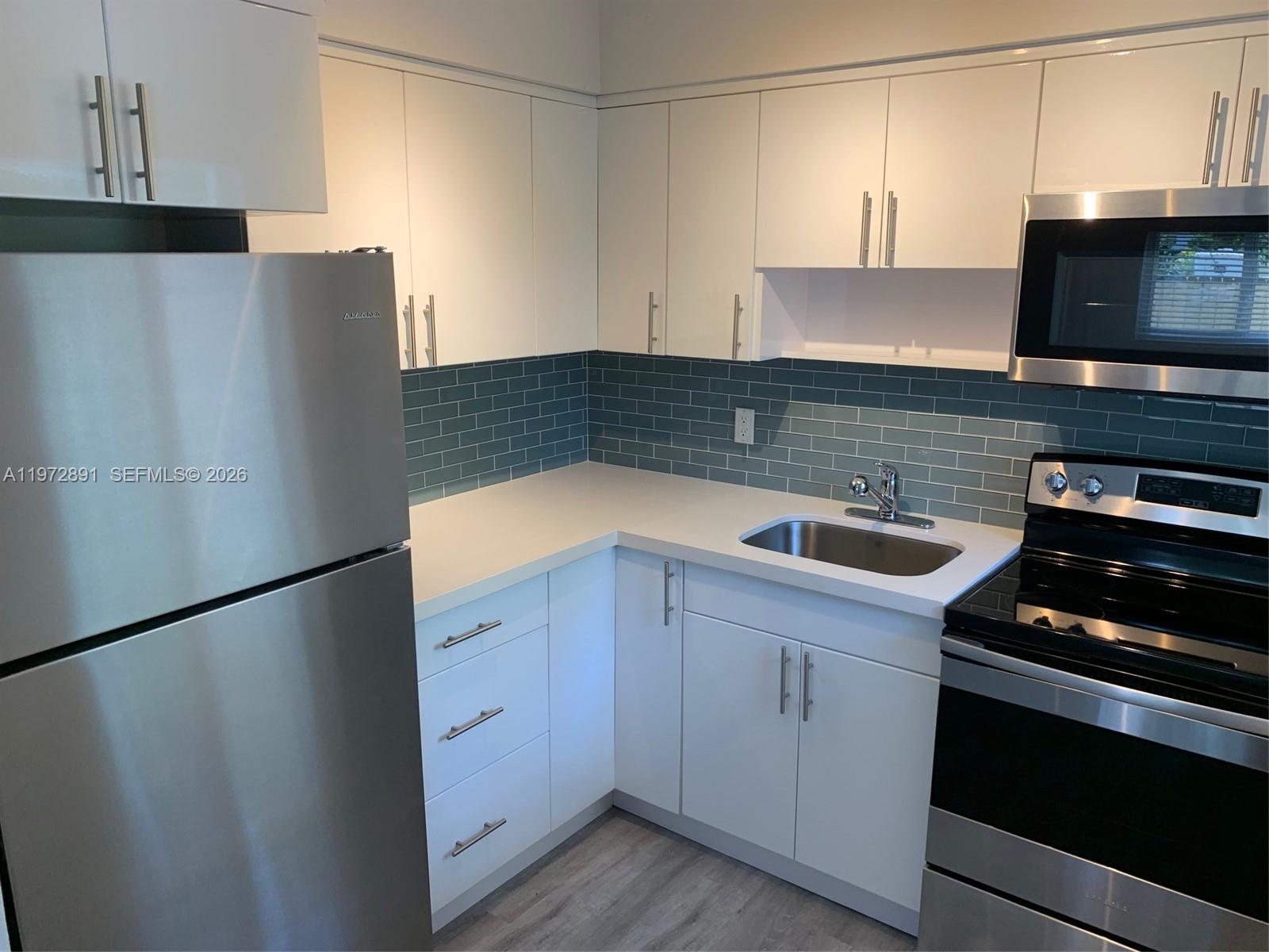 A kitchen features white cabinets, stainless steel appliances, a blue subway tile backsplash, and countertops — FORT LAUDERDALE, FL