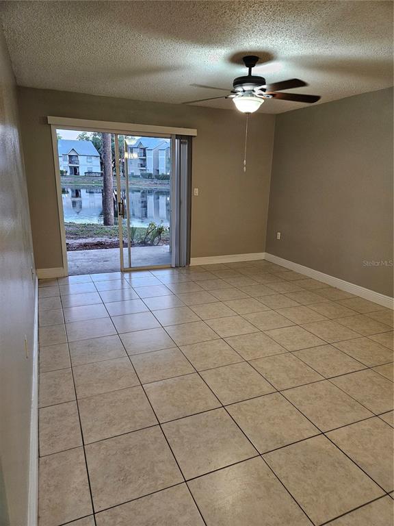 An empty room with beige tile flooring, a ceiling fan, and sliding doors to a patio — 1908 LAKE ATRIUMS CIRCLE UNIT 15, ORLANDO, FL