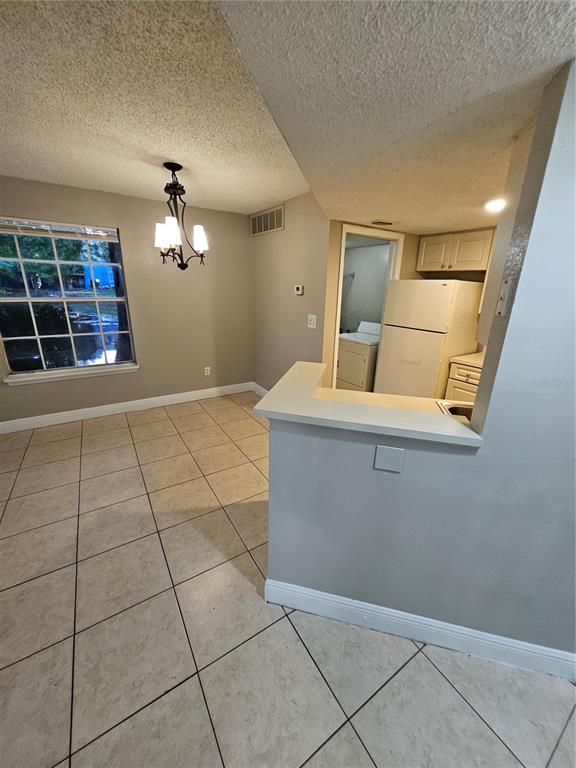 A dining area with tile flooring and a chandelier adjacent to a kitchen pass-through window — 1908 LAKE ATRIUMS CIRCLE UNIT 15, ORLANDO, FL