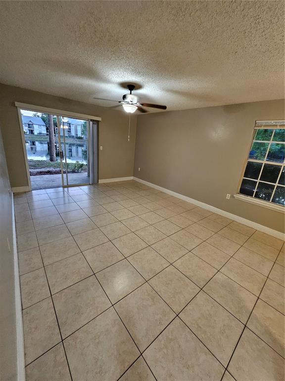 A living room with beige tile flooring, a ceiling fan, and sliding glass doors to a patio — 1908 LAKE ATRIUMS CIRCLE UNIT 15, ORLANDO, FL
