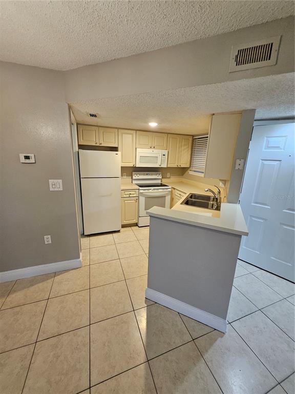 A kitchen with white appliances, light-colored cabinets, and tile flooring features a breakfast bar — 1908 LAKE ATRIUMS CIRCLE UNIT 15, ORLANDO, FL