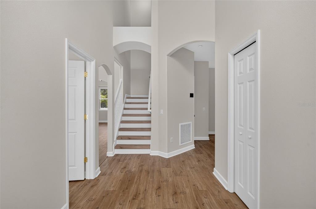 An entryway with wood-look flooring, a staircase, and white doors under a high ceiling — 166 W 11TH STREET, CHULUOTA, FL