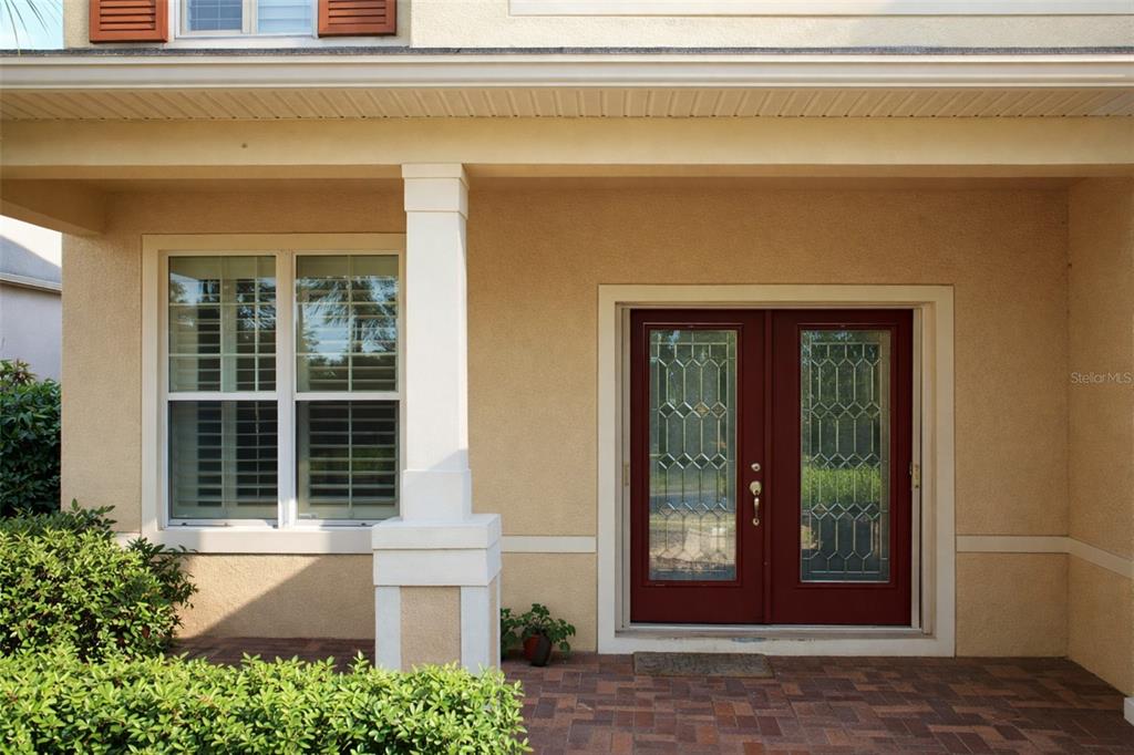 A beige house exterior features a brick patio, a white pillar, and double red doors — 1513 BALSAM WILLOW TRL, ORLANDO, FL