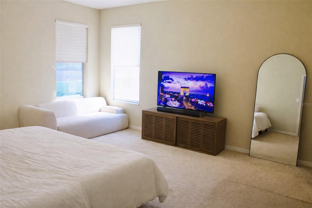 A bedroom features a bed, a white sofa, a television on a console, and a mirror — 1513 BALSAM WILLOW TRL, ORLANDO, FL