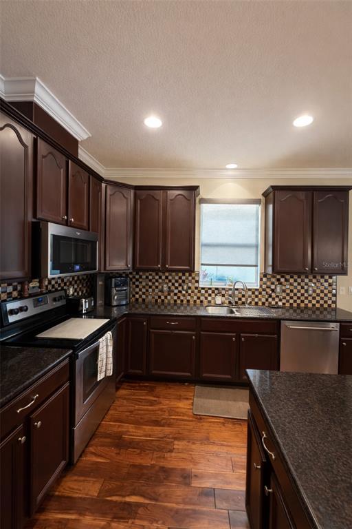 A kitchen features dark wood cabinets, granite countertops, a tiled backsplash, and hardwood flooring — 1513 BALSAM WILLOW TRL, ORLANDO, FL