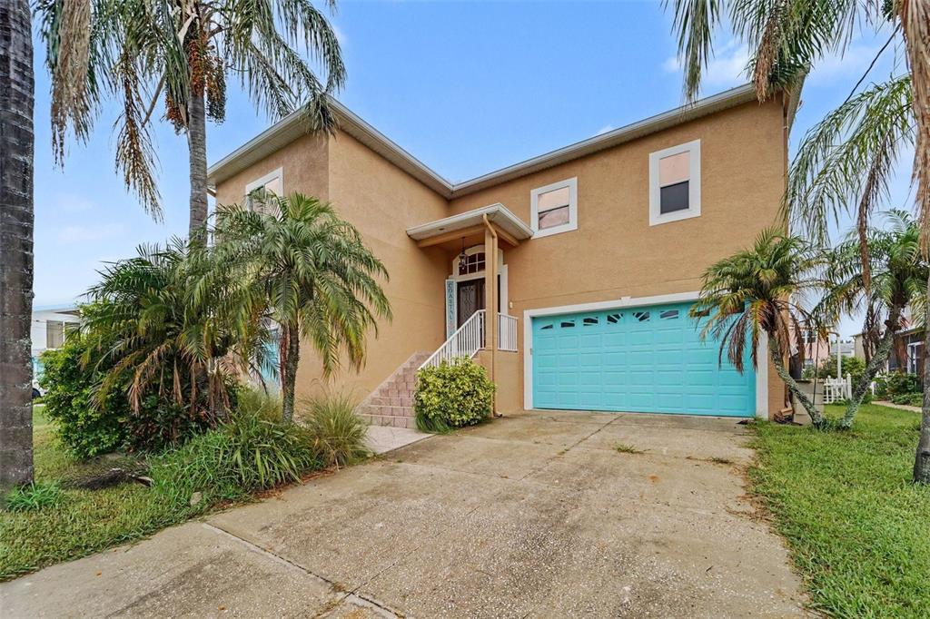 A two-story tan house features a bright turquoise garage door and a raised front entrance — 7533 HATTERAS DR, HUDSON, FL