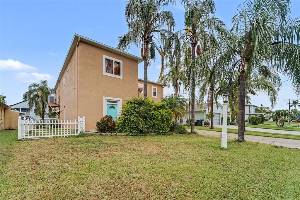 A two-story tan house with a white fence and palm trees in the front yard — 7533 HATTERAS DR, HUDSON, FL