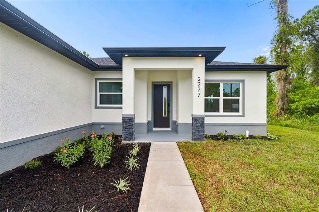 The exterior of a modern single-story house features a covered entryway with stone-accented pillars — 2277 SIMONTON AVENUE, NORTH PORT, FL