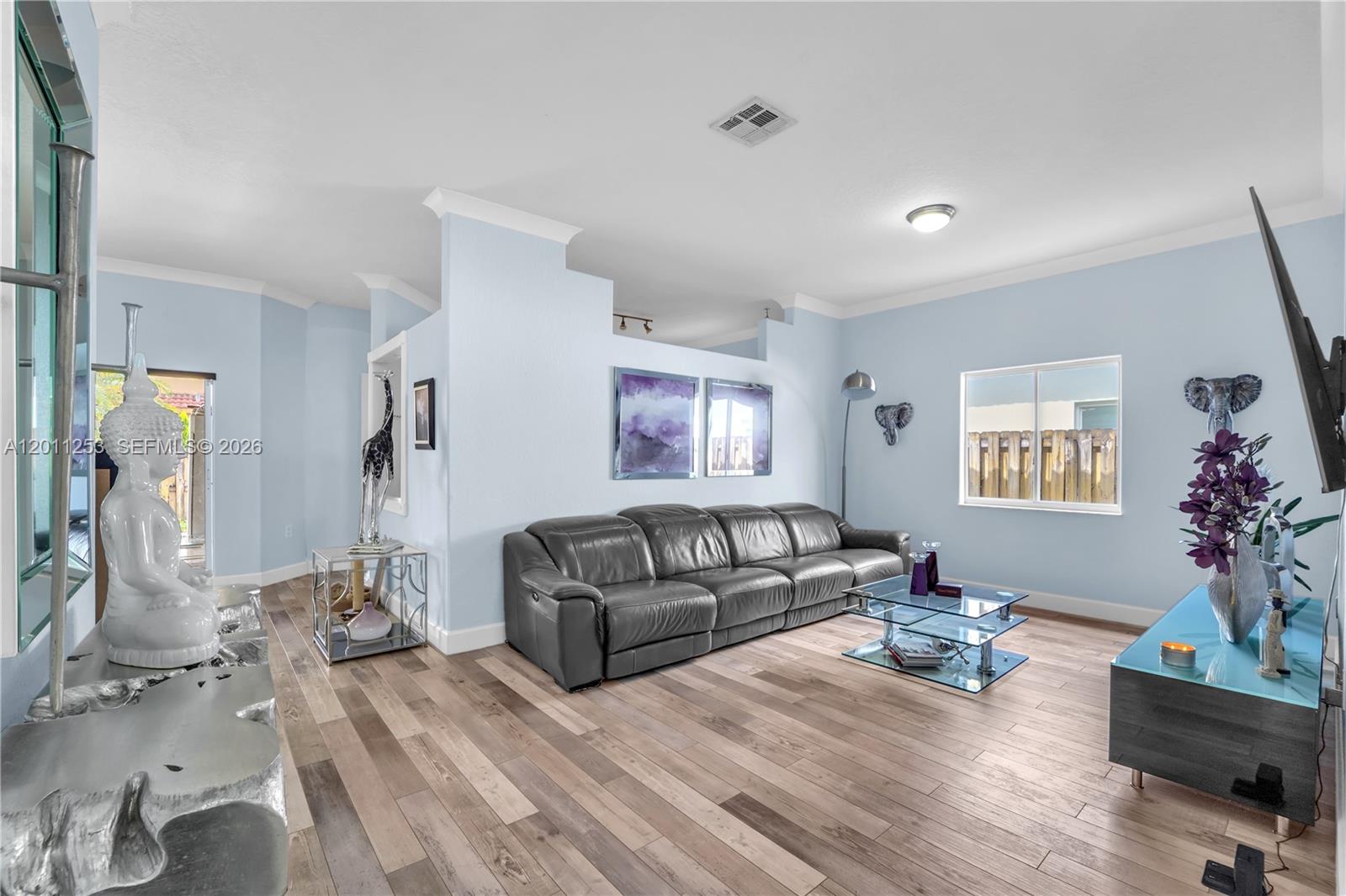 A living room features light blue walls, wood-look flooring, a gray sofa, and modern decor — 16266 SW 54th Ter # 0, Miami FL 33185, MIAMI, FL