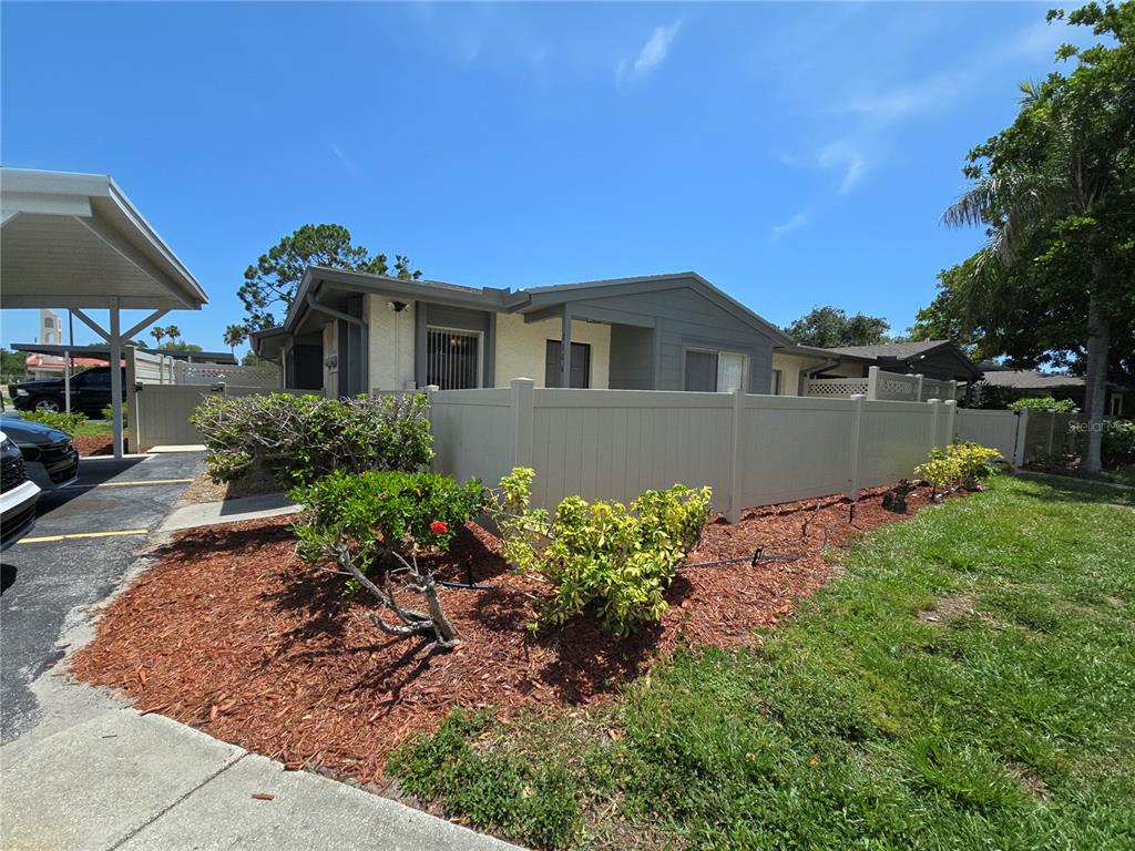 A single-story house with a tan fence, landscaped mulch beds, and a covered carport — 2606 29TH AVE W UNIT 12, BRADENTON, FL