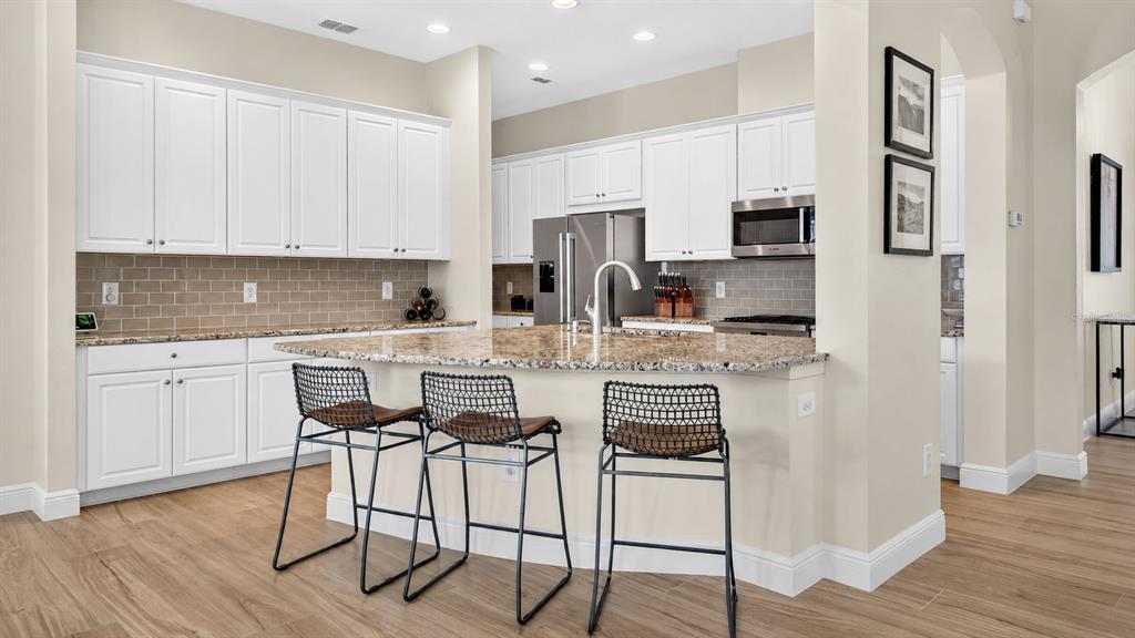 A kitchen features white cabinets, granite countertops, a tile backsplash, and three bar stools — 5954 CALDERA RIDGE DRIVE, LITHIA, FL