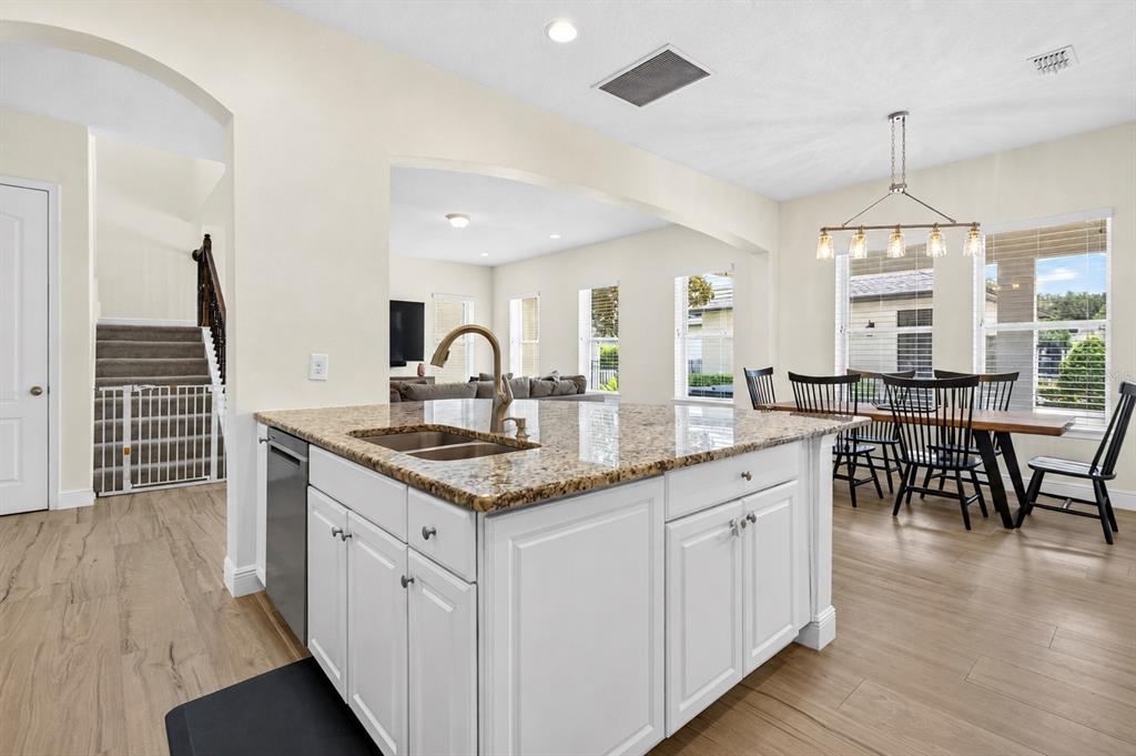 A kitchen island with granite countertops sits in front of a dining area and stairs — 5954 CALDERA RIDGE DRIVE, LITHIA, FL