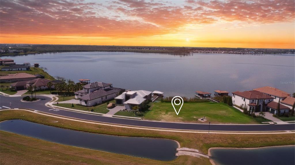 An aerial view shows a vacant waterfront lot situated between two large houses at sunset — 707 WATERFERN TRAIL DRIVE, AUBURNDALE, FL