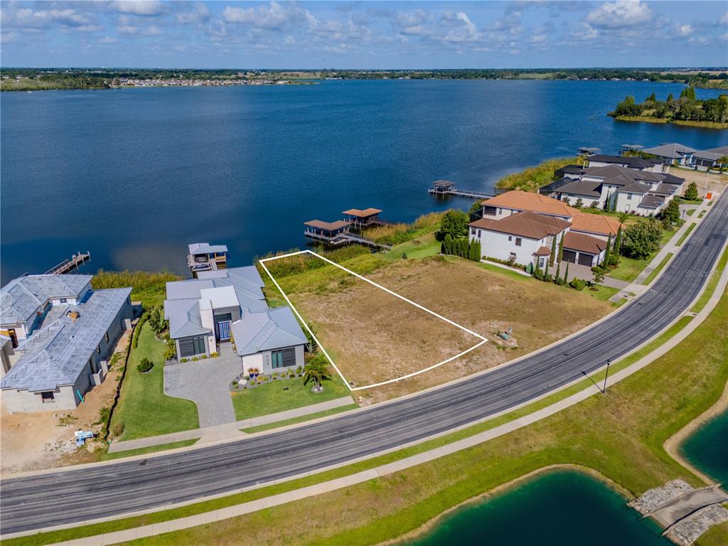 An aerial view shows a vacant waterfront lot outlined in white next to a modern house — 707 WATERFERN TRAIL DRIVE, AUBURNDALE, FL