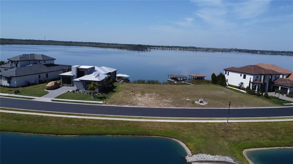 An aerial view shows a vacant waterfront lot situated between two large residential homes — 707 WATERFERN TRAIL DRIVE, AUBURNDALE, FL