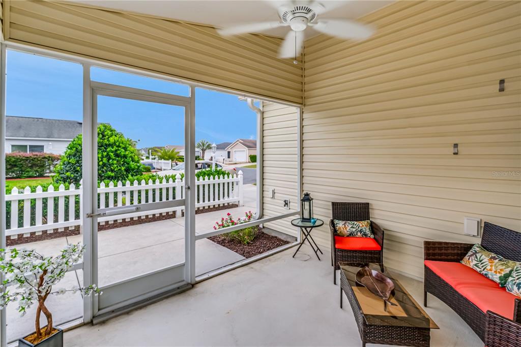 A screened-in patio features wicker furniture, a ceiling fan, and a view of a white fence — 1806 QUEENSBURY TERRACE, THE VILLAGES, FL