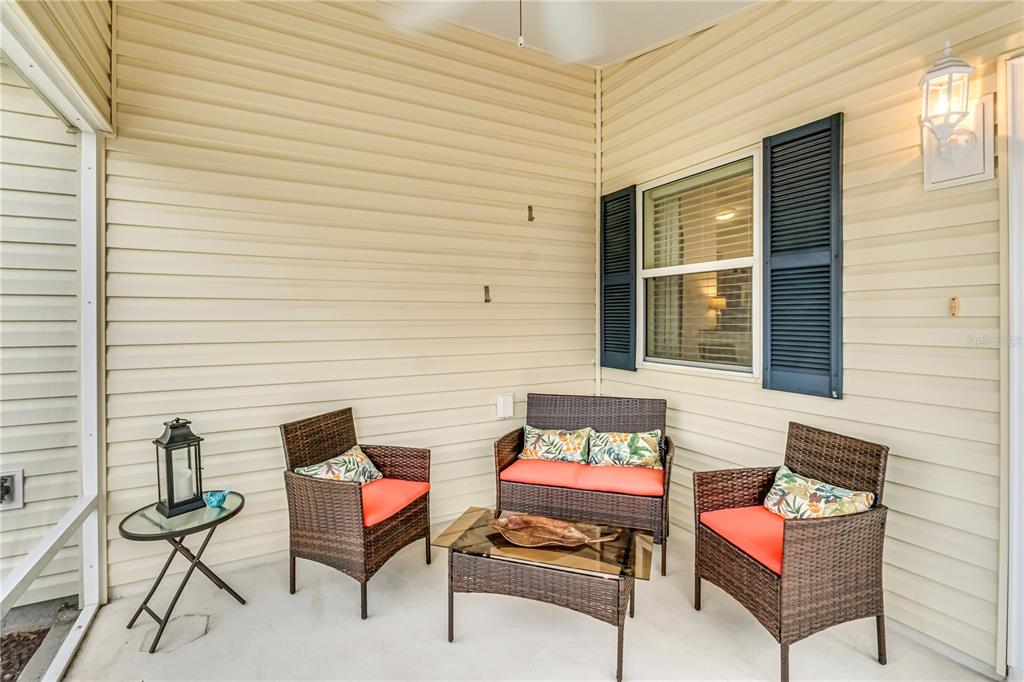 A covered patio features beige siding, a window with dark shutters, and wicker patio furniture — 1806 QUEENSBURY TERRACE, THE VILLAGES, FL
