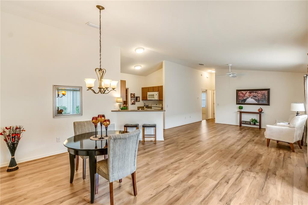 An open-concept dining area and living room featuring wood-look flooring and a kitchen breakfast bar — 1806 QUEENSBURY TERRACE, THE VILLAGES, FL