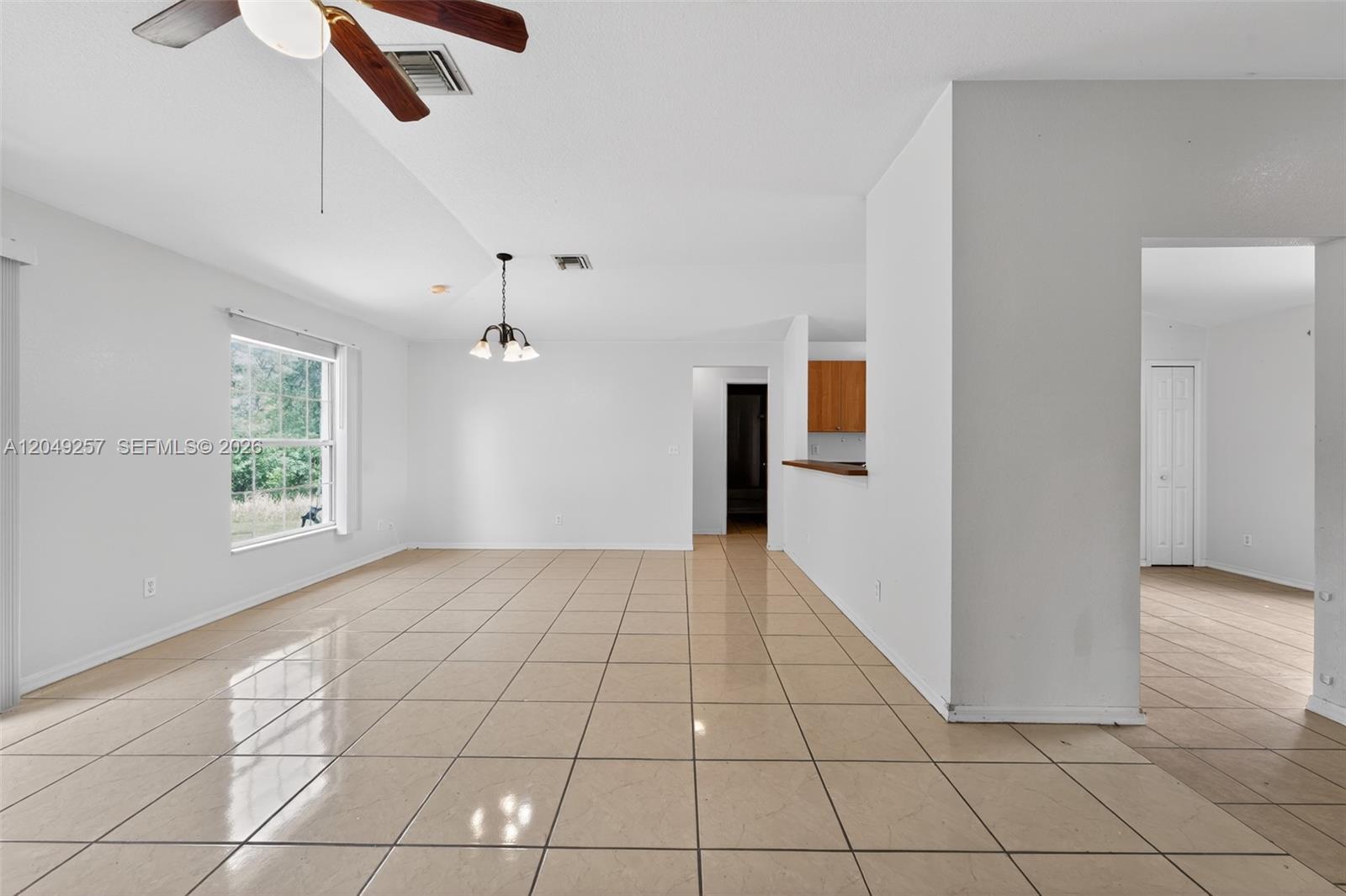 An open-concept living area features beige tile flooring, white walls, and a ceiling fan — 446 Windermere Dr., Lehigh Acres FL 33972, LEHIGH ACRES, FL