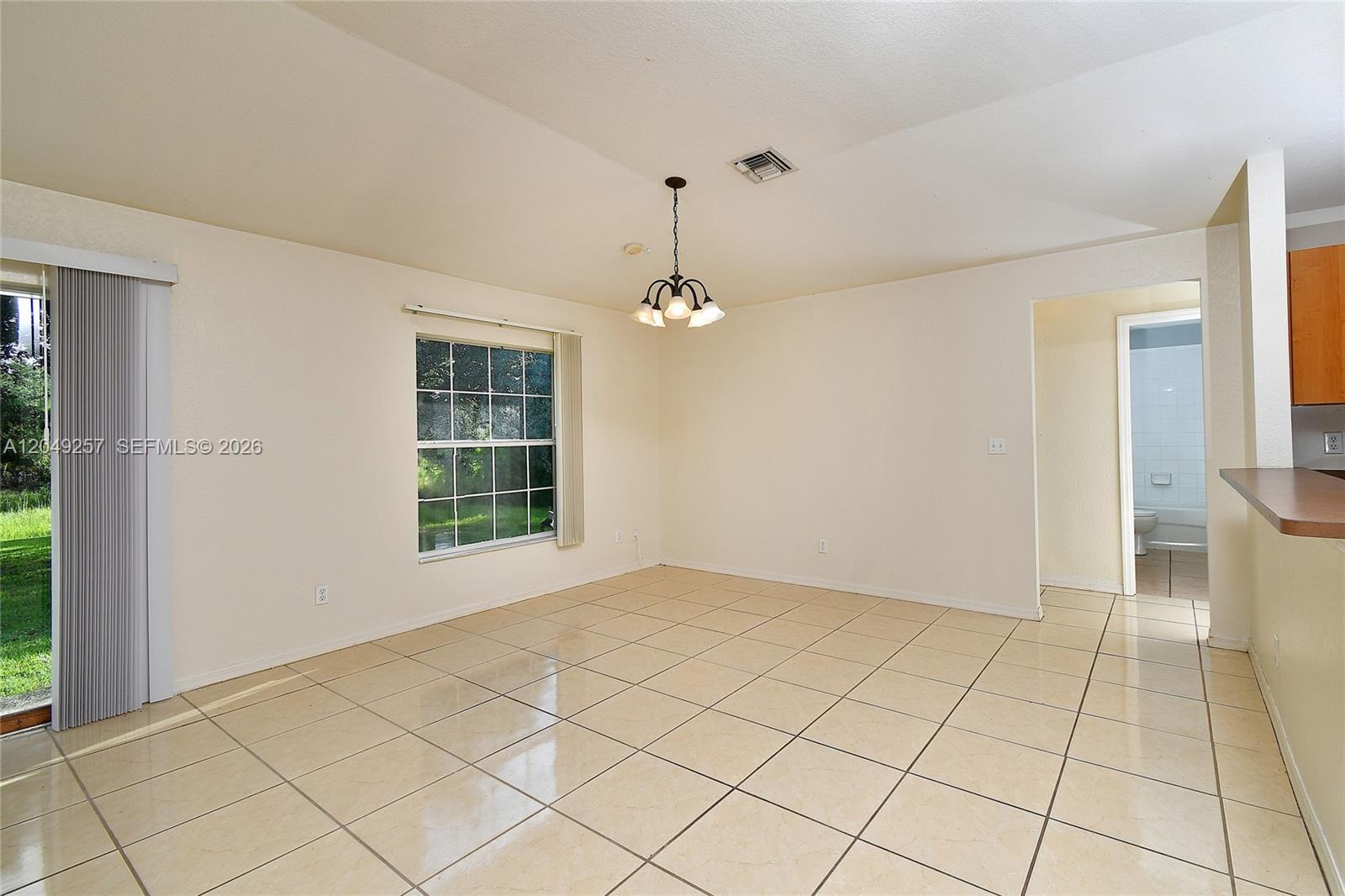 A dining area features beige tile flooring, a chandelier, and a sliding glass door — 446 Windermere Dr., Lehigh Acres FL 33972, LEHIGH ACRES, FL