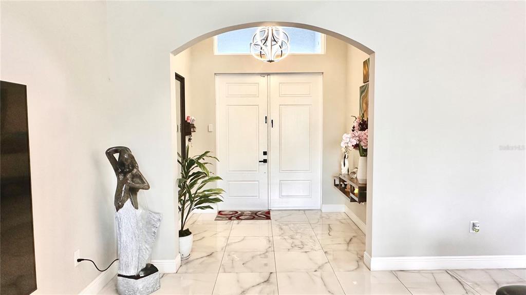 A bright entryway features white double doors, marble-look tile flooring, and an arched ceiling opening — 3900 21ST STREET SW, LEHIGH ACRES, FL