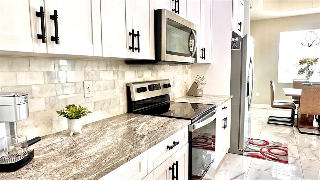 A kitchen features white cabinets, marble-look countertops, a tile backsplash, and stainless steel appliances — 3900 21ST STREET SW, LEHIGH ACRES, FL