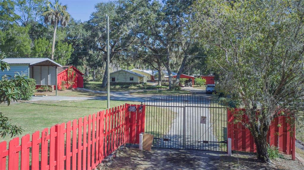 A red fence and metal gate open to a driveway leading toward several rural buildings — 11371 N HONEY JORDEN POINT, INGLIS, FL