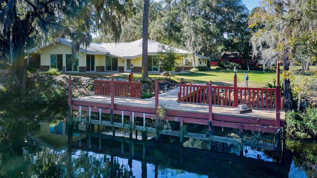 A yellow house with a metal roof sits behind a wooden dock on a canal — 11371 N HONEY JORDEN POINT, INGLIS, FL