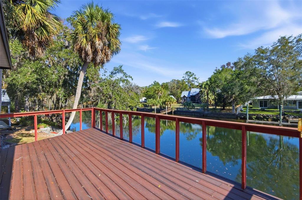 A wooden deck with a red railing overlooks a calm canal surrounded by trees — 11371 N HONEY JORDEN POINT, INGLIS, FL