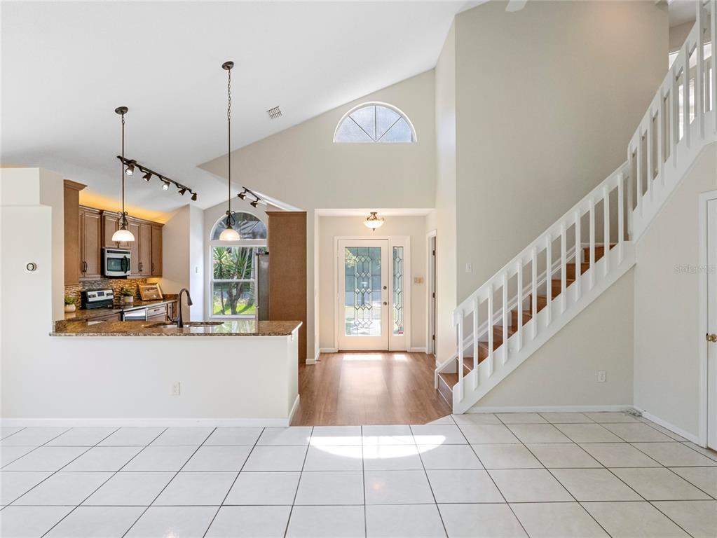A kitchen with granite countertops overlooks a foyer with a staircase and tile flooring — 416 SAND PEBBLE COVE, LONGWOOD, FL