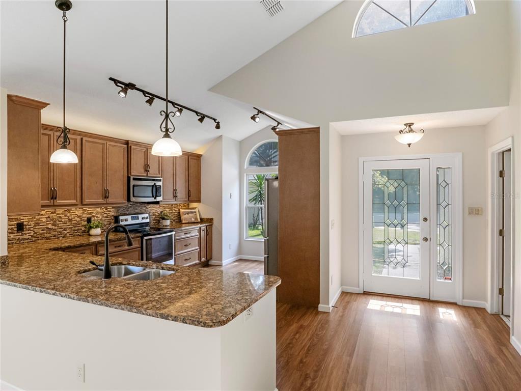 A kitchen with granite countertops and wood cabinets overlooks an entryway with a glass door — 416 SAND PEBBLE COVE, LONGWOOD, FL
