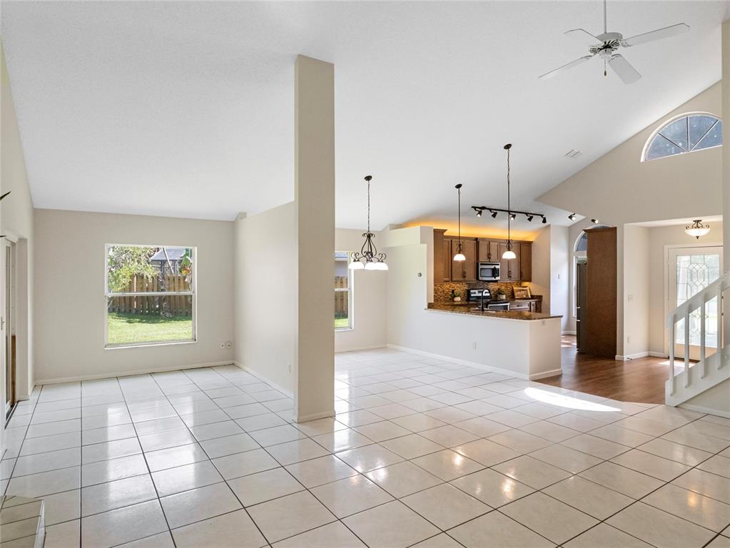 An open-concept living area features white tile flooring, a kitchen with wood cabinets, and vaulted ceilings — 416 SAND PEBBLE COVE, LONGWOOD, FL