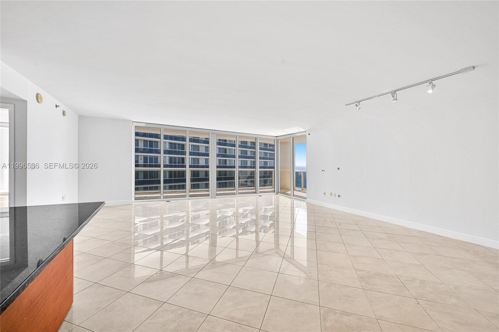An empty living area features large windows, light-colored tile flooring, and a track lighting system — 1850 S Ocean Dr # 3510, Hallandale Beach FL 33009, HALLANDALE BEACH, FL
