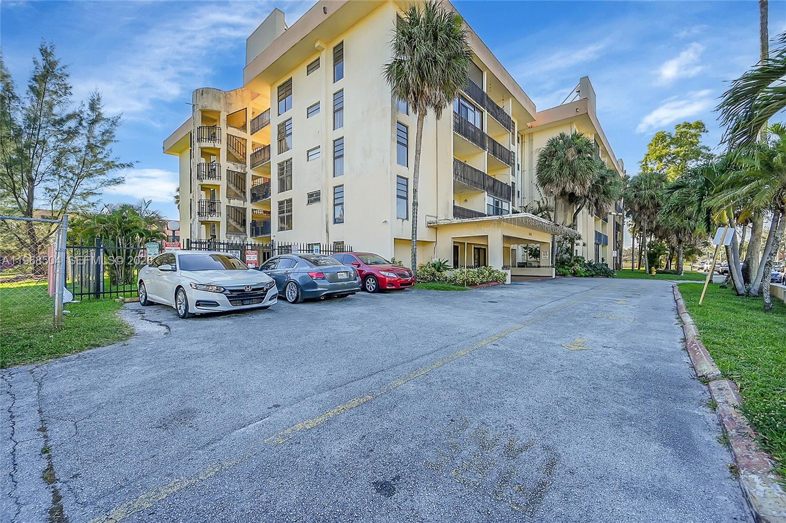 A multi-story yellow apartment building features a parking lot with three cars in front — 650 NE 149th St # 406A, Miami FL 33161, MIAMI, FL